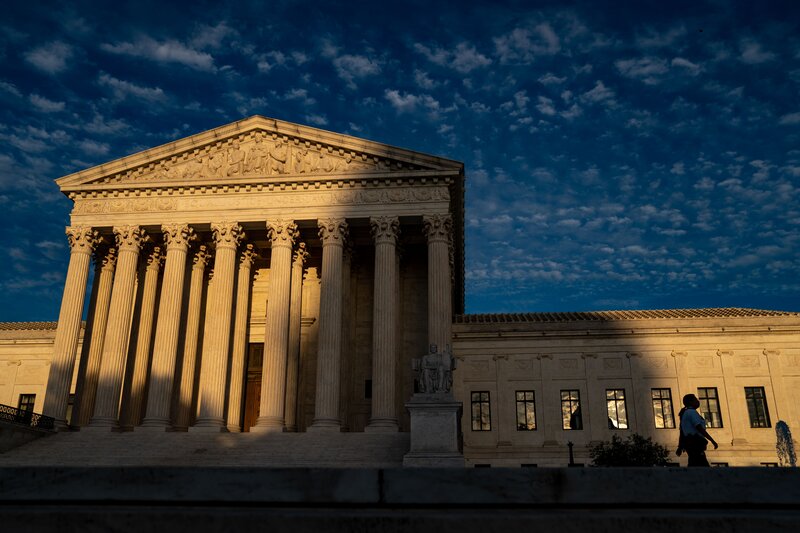 The columned entrance of a grand courthouse is seen in shadows beneath a twilit sky